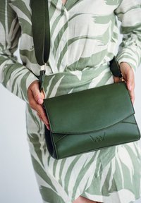 Zelená kožená kabelka na rameno s klopou, s dekorativním švem a zlatými kovovými doplňky. Strukturální povrch; kompaktní obdélníkový tvar.