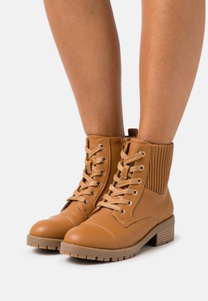 Bottines couleur fauve en cuir lisse avec un panneau en tissu côtelé, bout rond et fermeture à lacets. Elles présentent un talon carré et une semelle texturée.