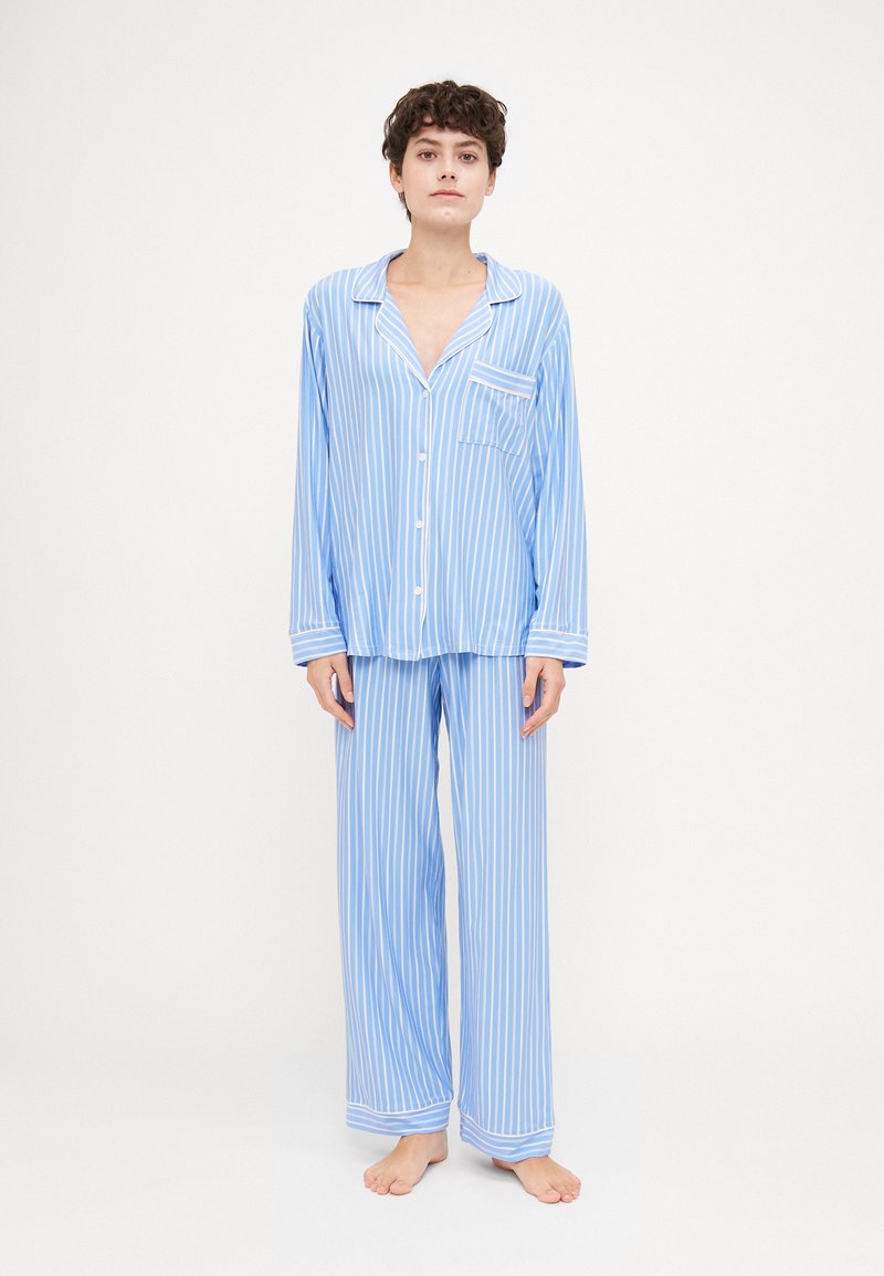 Conjunto de pijama listrado em azul claro feito de tecido suave. Camisa de botão de manga longa com bolso no peito e calças largas combinando.