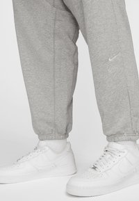 Grå bomulds sweatpants med elastiske manchetter, parret med hvide læder Nike sneakers med perforerede detaljer og logo. 