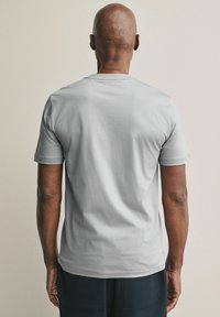 Grijze t-shirt met korte mouwen, van katoen, ronde hals, relaxte pasvorm, eenvoudig ontwerp, geen zichtbare patronen, gedragen met marineblauwe broek, gezien van de achterkant.