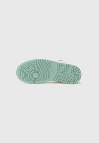 Sneakersåle i lys grøn gummi, tekstureret med cirkulære og lineære mønstre, med et centralt logodetalje.