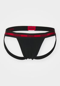 Schwarzer Stoff-Thong mit gerafftem Vorderteil, ausgestattet mit elastischen roten und schwarzen Taillenbändern, die das "HUGO"-Branding tragen.