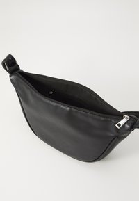 Melnas ādas soma ar izliekta formu, augšējo rāvējslēdzēju un gludu tekstūru. Iekļauj sudraba rāvējslēdzēja vilkšanas elementu un iekšējo kabatu.