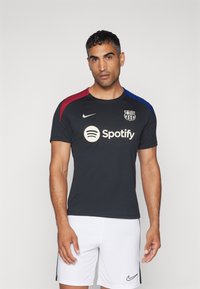 Sort Nike fodboldtrøje med røde og blå detaljer på skuldrene, med Spotify-logoet og Barcelona klubmærket. Hvide shorts.