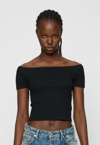 Top scurt negru, cu umerii descoperiți, textură ribbed, mâneci scurte, asortat cu blugi din denim ușor albastri, cu talie înaltă.