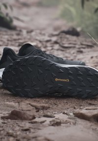 Suola nera di scarpa sportiva con motivo Continental su superficie rocciosa di sentiero esterno.