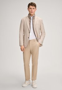 Beżowa lniana marynarka z szarym pikowanym kołnierzem, biała koszula i beżowe spodnie w połączeniu z białymi tenisówkami. Prosty fason i dopasowany krój.