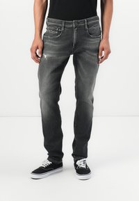 Jeanși negri de denim ușor decolorati, cu croi drept, având un model uzat și buzunare frontale. Asortați cu adidași negri.