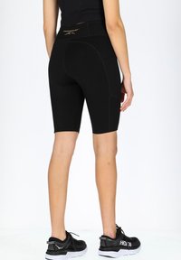 Svarta cykelbyxor med en åtsittande design, med hög midja och synlig sömnad. Matchas med svarta träningsskor.
