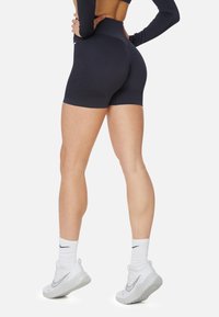 Hochtaillierte dunkelgraue Sportshorts mit einem strukturierten Design, kombiniert mit weißen Turnschuhen und knöchellangen Socken, von hinten betrachtet.