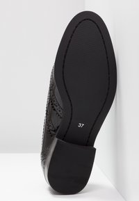 Semelle de chaussure en cuir noir avec une finition lisse et texturée, présentant des éléments de design perforés et une taille estampillée 37.