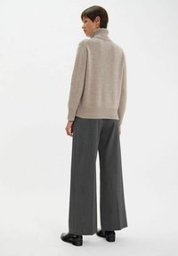 Pull en maille beige avec un col montant, associé à un pantalon large à rayures grises et des chaussures noires ; texture lisse dans l'ensemble.