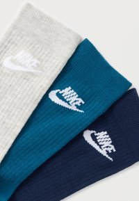 Három pár zokni szürke, türkiz és tengerészkék színben. Mindegyiken bordázott textúra és egy fehér, jól látható Nike logó található.