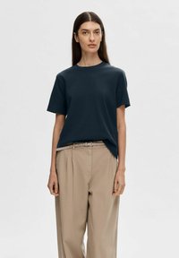 Dark blue cotton t-shirt with short sleeves, a round neckline, and a relaxed fit, paired with high-waisted beige trousers.