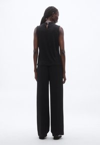 Fekete ujjatlan felső kulcslyuk részlettel a háton; széles szárú fekete nadrággal párosítva. Sima textúra, visszafogott dizájn.