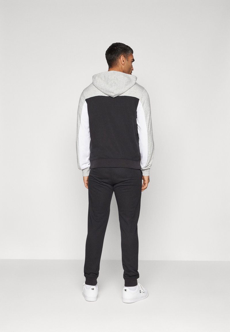 Felpa con cappuccio nera e grigia con accenti bianchi sulle maniche, design aderente, texture morbida e polsini elasticizzati, indossata con pantaloni della tuta abbinati.