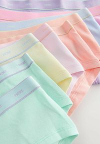 Sedem parov bombažnih spodnjih perilo pastelnih barv, lepo zloženih v vrsto, vsak s trakom z blagovno znamko.