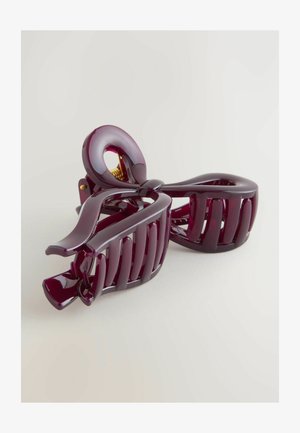 Lilla plastik hårklemme med bue-design, der har en blank finish, kurvet form og sammenkoblede tænder for et sikkert greb. Guld metalbeslag synligt.