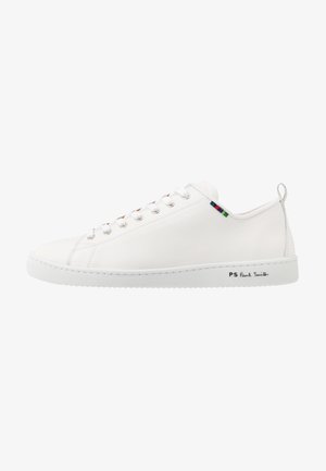 Vita lädersneakers med en slät yta, rund tå och kontrasterande färgad randdetalj nära snörningen. Har en gummisula och varumärkeslogotyp på sidan.