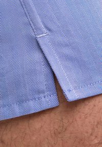 Tissu rayé bleu et blanc avec un motif en chevrons, avec un ourlet net et des coutures visibles aux bords. Texture douce.