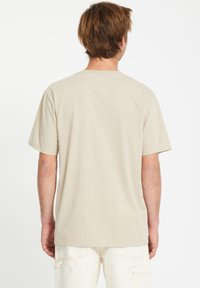 Beige katoenen t-shirt met korte mouwen en een ronde halslijn, met een gladde textuur en een losse pasvorm, weergegeven vanaf de achterkant.