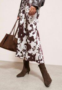 Rudos ir baltos spalvos raštuotas maxi sijonas, rudi zomšiniai bateliai iki kulkšnies su smailiu noseliu ir atitinkanti ruda zomšinė rankinė.