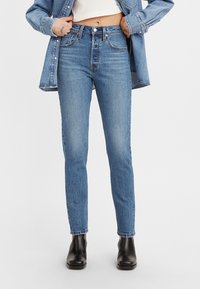 Úzké modré džíny z denimu s vysokým pasem, minimálním vyblednutím a designem s pěti kapsami, doplněné černými kotníkovými botami.