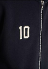 Navy blue zipper jacket with white embroidered number 10 on the left chest area.