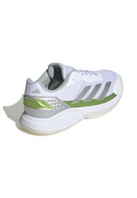 Weißer Sportschuh mit einem strukturierten Mesh-Obermaterial, grauen Akzenten, einem glänzenden grünen Fersendetail und einer Gummisohle mit wellenförmigem Muster.