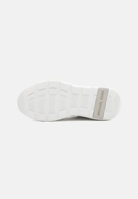 Talon de sneaker alb din cauciuc, cu striuri orizontale și verticale pentru aderență, având un accent rectangular metalic pe care scrie "MICHAEL KORS."