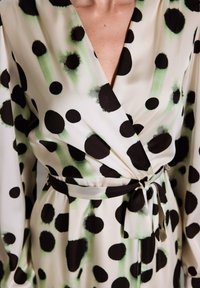 Robe portefeuille en tissu léger, ornée de grands pois aquarelle noirs et verts sur un fond crème, avec une ceinture nouée à la taille.