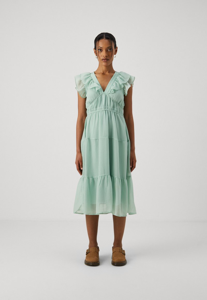 Heled minta roheline, kihiline kleit rippuvate lühikeste varrukatega, V-dekoltee ja kogutud vöökohaga. Kerge kangas, äär ulatub põlvest allapoole.