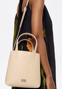 Beige textured leather handbag with dual handles and a removable shoulder strap, featuring branding at the front.