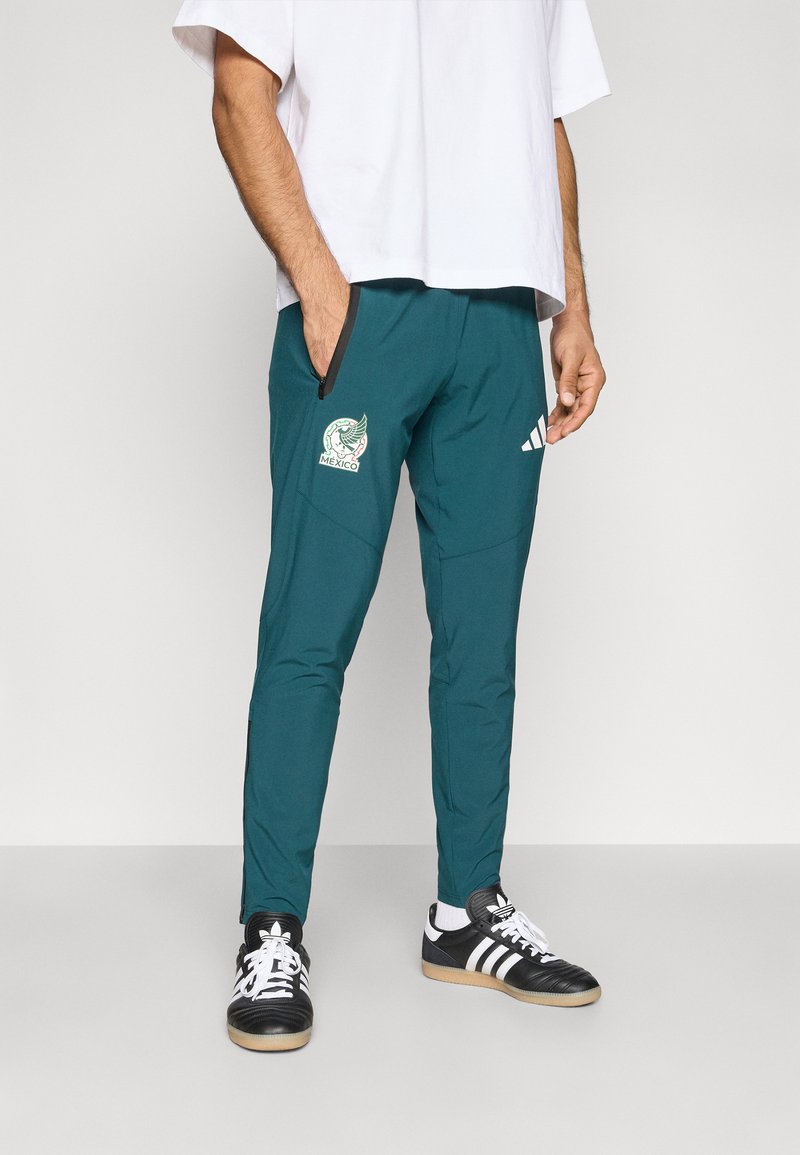 Türkiz atlétikai nadrág cipzáras zsebbel, Mexikó csapatlogójával a bal lábszáron és fehér Adidas csíkokkal a jobb oldalon.