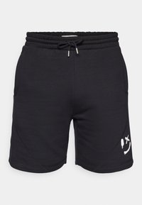 Shorts de sport noirs en tissu doux, dotés d'une taille élastique avec cordon de serrage, de poches latérales et d'un motif graphique blanc au niveau de l'ourlet.