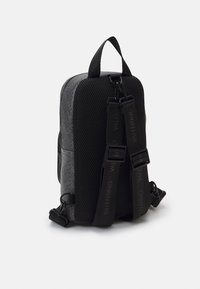 Black mesh backpack with logo pattern, featuring a simple shape, adjustable straps, and a top handle for easy carrying.