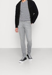 Vaqueros ajustados grises, camiseta de rayas azul marino y blanco, y chaqueta de pana negra. Zapatillas en blanco y negro completan el conjunto.