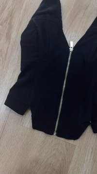 Zwarte ritssluitingjack met gestructureerde schouders, lange mouwen en een metallic rits. Het materiaal lijkt glad met een slim fit en zonder zichtbare patronen.
