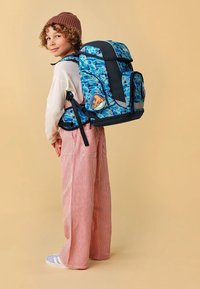 Sac à dos bleu à motifs avec des accents noirs, plusieurs compartiments et un badge rond présentant un design de pieuvre. Tissu texturé.
