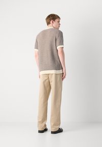 Gray knit short-sleeve sweater with cream trim, paired with beige trousers. Texture is breathable; silhouette is loose-fitting.