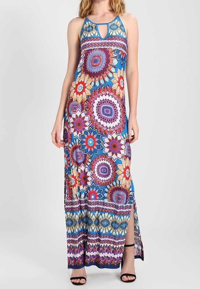 Femme portant une robe maxi sans manches colorée avec de grands motifs floraux circulaires et une fente latérale, associée à des talons ouverts noirs.