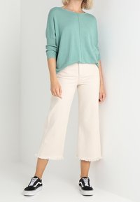 Ljus teal färgad stickad tröja med rund halsringning, tillsammans med beige avkortade byxor med fransade fållar och svarta sneakers.