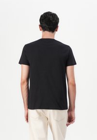 T-shirt en coton noir à manches courtes et col rond, présenté de dos. Design simple sans logos ni motifs visibles.