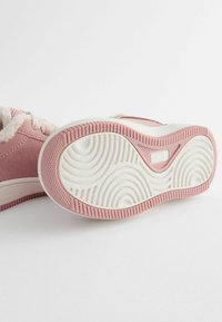 Rosa mockaskor med vit, fluffig foder, gummisula med vågmönstrade spår och en texturerad rosa och vit botten.