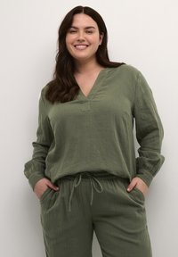 Grünes, strukturiertes zweiteiliges Outfit mit V-Ausschnitt und langen Ärmeln. Das Oberteil hat eine lockere Passform; die Hose hat einen Kordelzugbund und Seitentaschen.