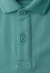 Nahaufnahme eines türkisfarbenen Poloshirt-Kragens mit zwei zugeknöpften Knöpfen und detaillierter Naht an der Knopfleiste.