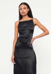 Mustmust kleid otse dekolteega, õhukeste rihmadega ja voogeldusega siluetiga. Sile tekstuur kerge läikega ja ilma nähtavate mustriteta.