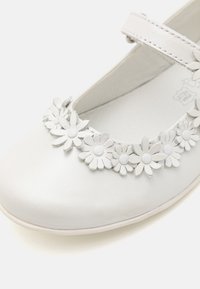 Witte leren Mary Jane-schoen met een bloemenversiering aan de voorkant, met lichtgrijze bloemblaadjes en ronde accenten. Glad oppervlak.