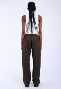 Bruine broek met wijde pijpen van katoen, met een achterzak en een hoge taille, gecombineerd met een witte mouwloze top.
